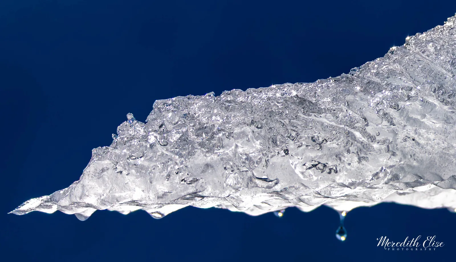 Close-up of crystalline melting ice with a single hanging water droplet against deep blue — Nunavut Canada fine art print