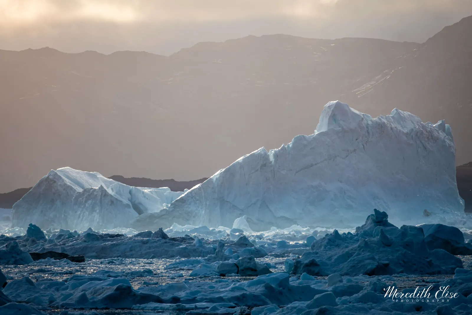 Backlit iceberg glowing at golden hour amid sea ice beneath barren mountains — Greenland fine art print